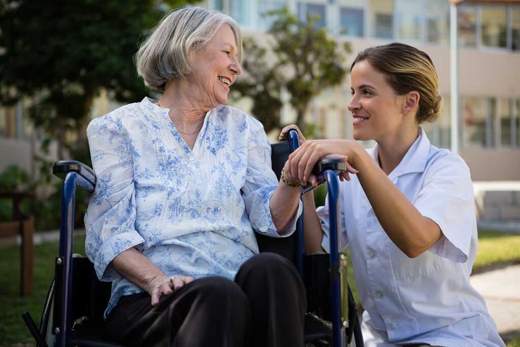 Two older adults seated at a dining table choosing meals from a menu with a caregiver nearby, emphasizing choice and respect.
